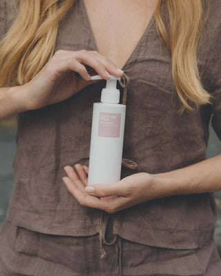 Ein weißer Pumpspender mit rosa Etikett der Phametra Schutz und Pflege Waschlotion für den Intimbereich wird vor dem oberen Torso einer Frau mit roten Haaren gehalten.