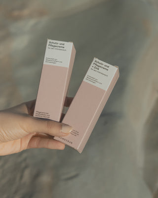Eine weibliche Hand hält zwei pinke, rechteckige Verpackungen vor einem Hintergrund aus Stein