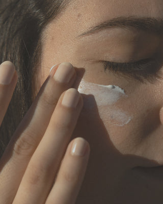 Brunette Frau schmiert sich mit Fingern Sonnencreme ins Gesicht
