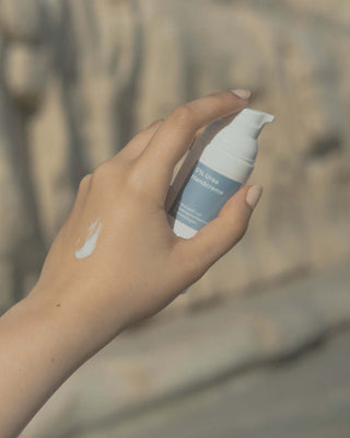 Eine weibliche Hand mit einem Kleks Handcreme hält einen blau-weißen Handcremespender