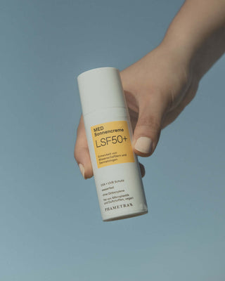 Eine Hand hält einen weiß-gelben Spender mit Phametra Sonnencreme ins Wasser