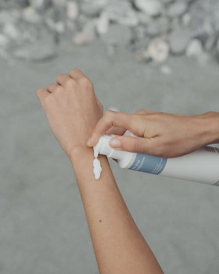 Die 5 % Urea Bodylotion von in einem weißen Pumpspender mit blauem Etikett wird auf einen Arm aufgetragen.