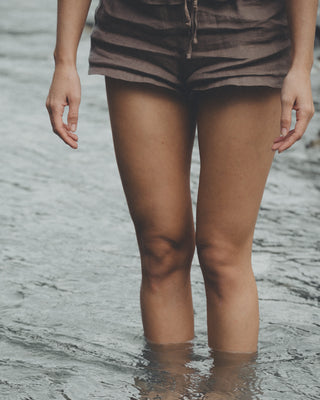 Nahaufnahme von Beinen einer Frau, welche in einem Fluss steht, wo ihr das Wasser bis unter die Knie reicht. 