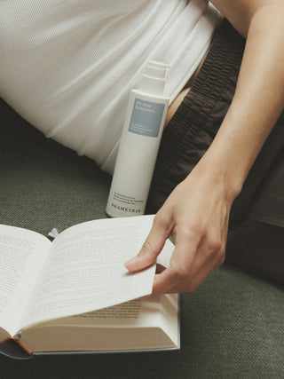 Die 5 % Urea Bodylotion liegt auf dem Sofa während eine Frau ein Buch liest
