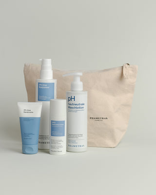 Hellbrauner Baumwoll-Kosmetikbeutel mit einem schwarz umrandeten Herz und Aufschrift "the kindest gift? care." Davor stehen 4 blaue Hautpflege-Produkte von Phametra Cosmetics.