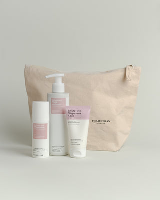 Hellbrauner Baumwoll-Kosmetikbeutel mit einem schwarz umrandeten Herz und Aufschrift "the kindest gift? care." Davor stehen 3 pinke Intimpflege-Produkte.