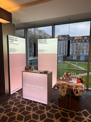 Pink-weiße Messestände von Phametra Cosmetics stehen auf einem gemusterten Teppich und vor einer Fensterfront