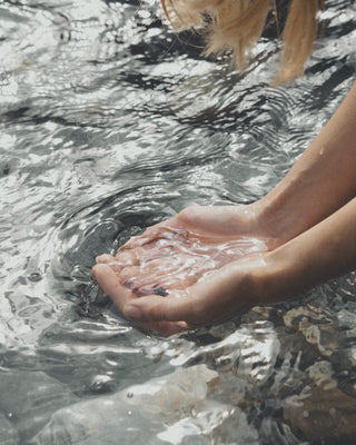 Nahaufnahme weiblicher zusammengefaltener Hände, die Wasser aus einem Fluss schöpfen.