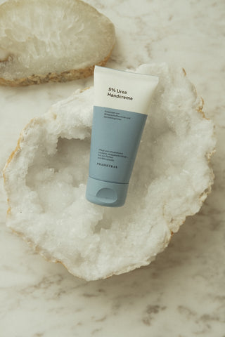 Eine blau weiße Tube mit Phametra Cosmetics 5 % Urea Handcreme liegt auf einer Geode.