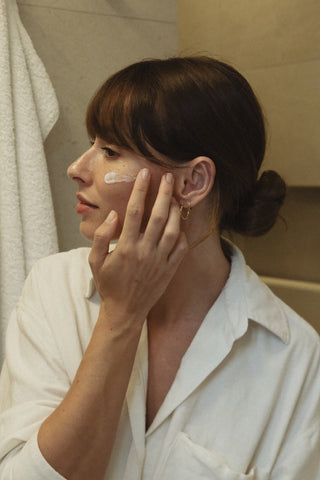 Eine brunette Frau cremt sich das Gesicht mit Phametra Cosmetics Med Gesichtscreme im Badezimmer ein