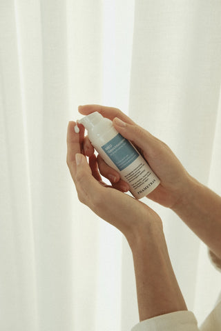 Zwei weibliche Hände halten den blau-weißen Pumpspender mit Phametra Cosmetics Gesichtscreme vor weißem Hintergrund