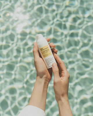 Medizinische Sonnencreme wir in zwei Händen gehalten. Im Hintergrund ist ein Pool zu sehen.