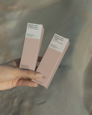 Hand hält zwei rosa Verpackungen der Phametra Schutz- und Pflegecreme für den Intimbereich, eine davon mit Zink, entwickelt von Wissenschaftlern und Dermatologen für empfindliche Haut
