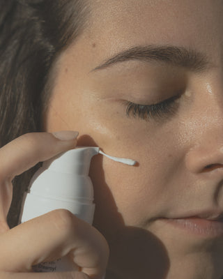 Eine brunette Frau gibt mit einem weißem Pumpspender Sonnencreme auf die Wange