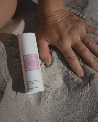 Phametra Schutz- und Pflegecreme für den Intimbereich in weißem Pumpspender auf Sand neben einer Hand, entwickelt von Wissenschaftlern und Dermatologen, frei von Mikroplastik und Duftstoffen
